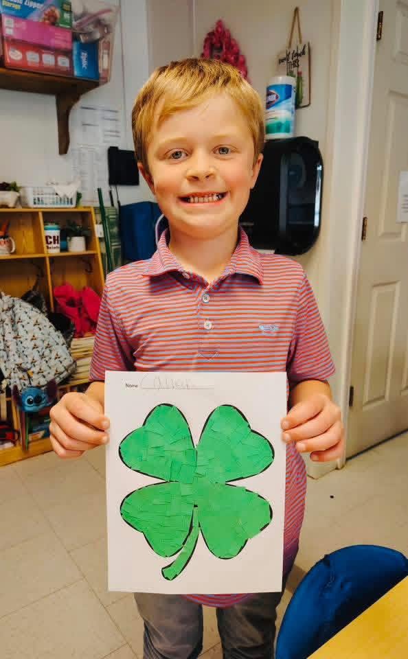 A smiling Clarendon Hall student proudly showing a green paper art project